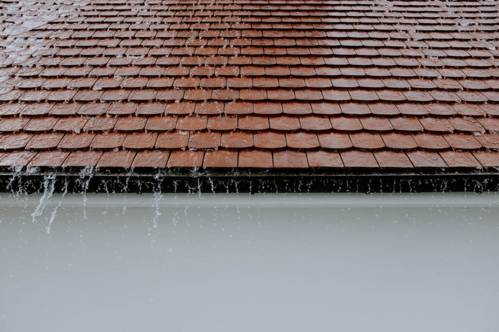A residential roofing system with rain pouring on top of it.